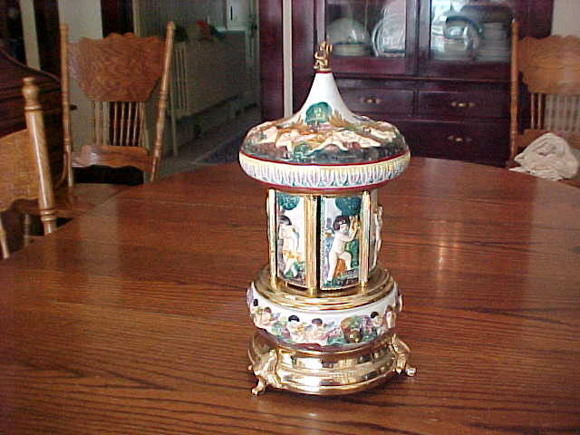 Sold at Auction: Vintage musical carousel lipstick/cigarette holder, with  warriors and maidens on porcelain panelled doors and chariots on roof,  topped by metal cherub. Hand painted. On tri-footed metal base. Approx 34cm